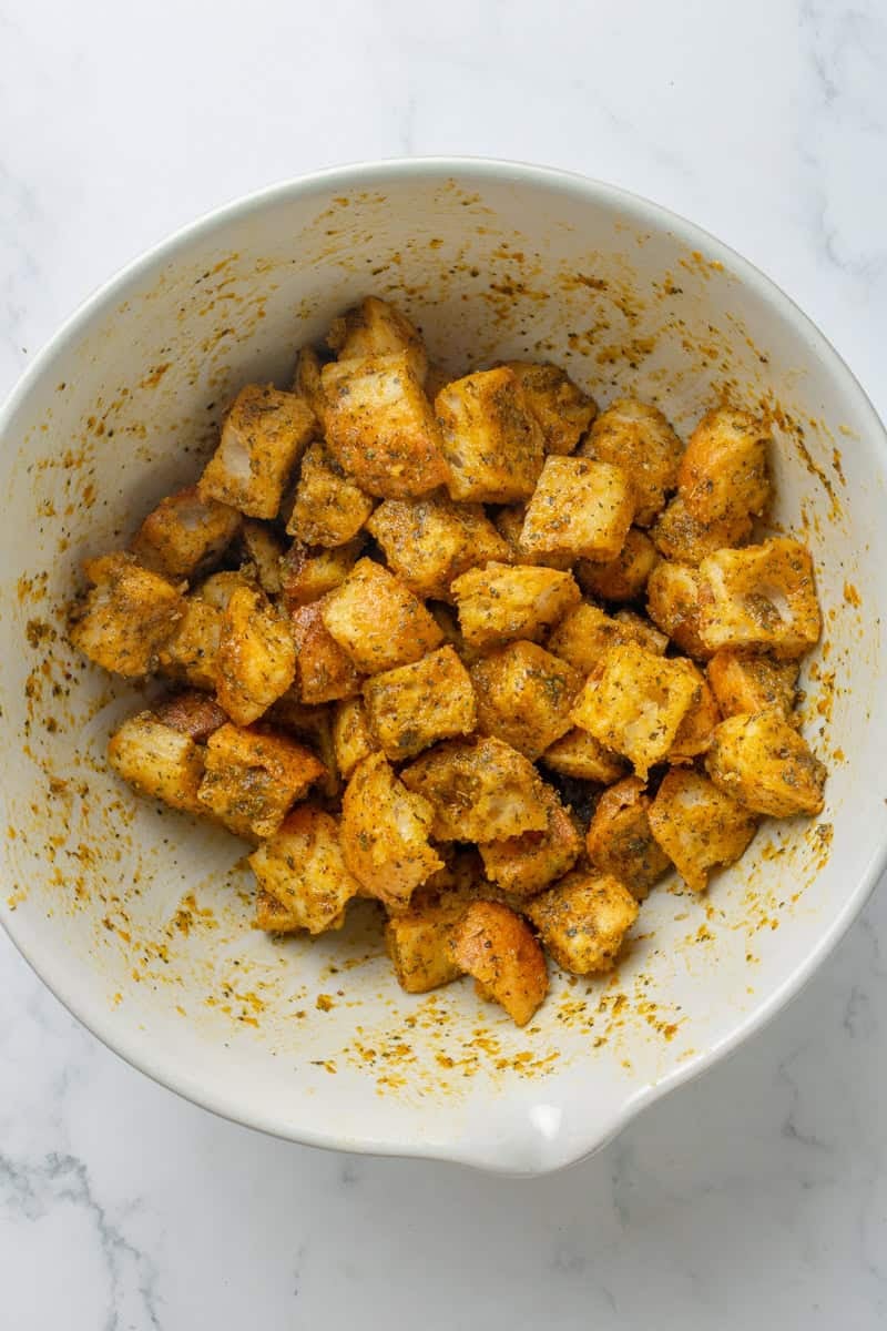 Seasoned uncooked croutons in a white bowl.