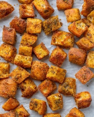 Golden seasoned baked homemade croutons on a lined baking pan.