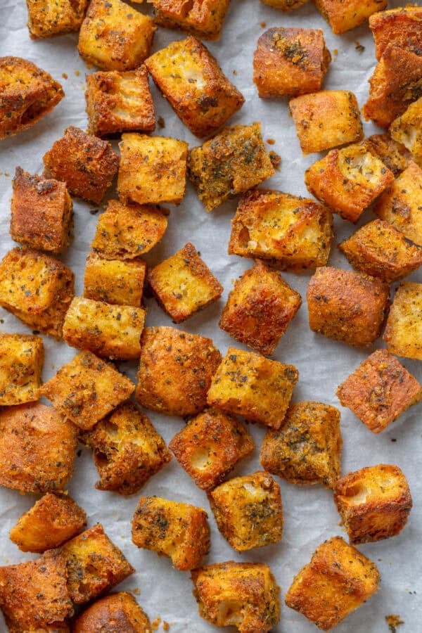 Golden seasoned baked homemade croutons on a lined baking pan.