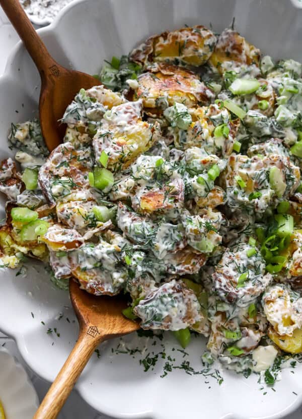 Creamy crispy potato salad with fresh herbs in a large bowl with wood serving spoons in it.