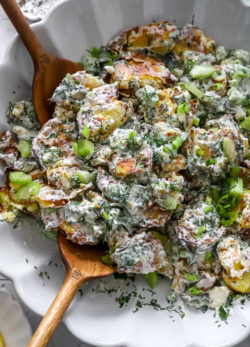 Creamy crispy potato salad with fresh herbs in a large bowl with wood serving spoons in it.