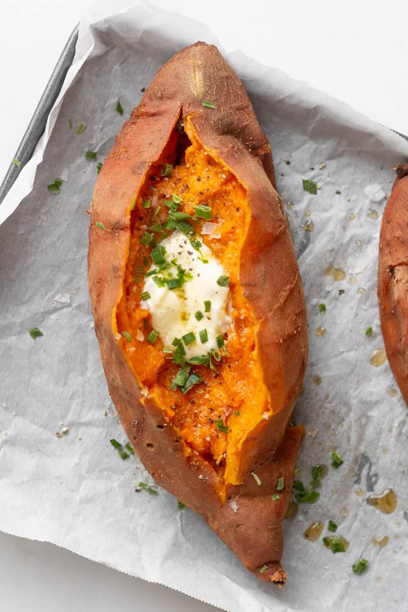 Cooked instant pot sweet potato sliced with butter and chives on it with another one next to it.
