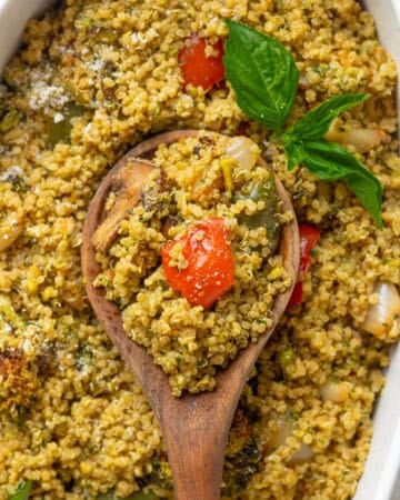 Wooden spoon with cooked seasoned quinoa on it with more behind it in a casserole dish.
