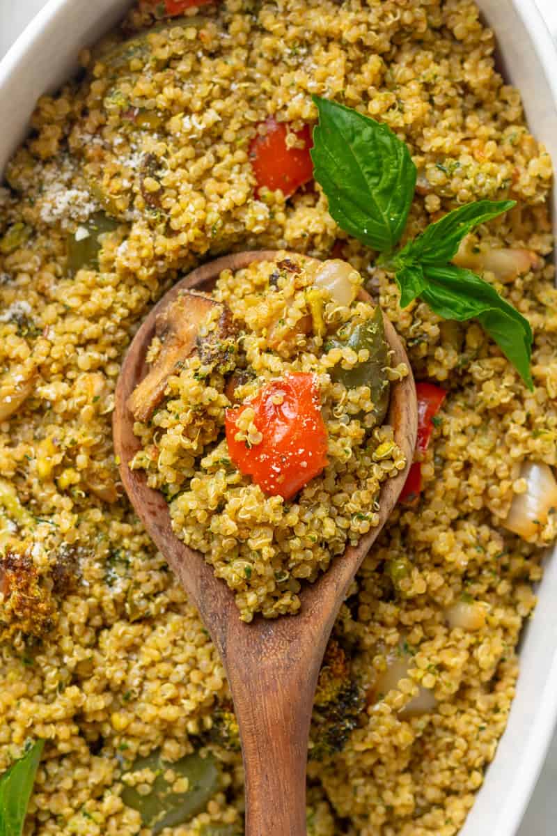 Wooden spoon with cooked seasoned quinoa on it with more behind it in a casserole dish.