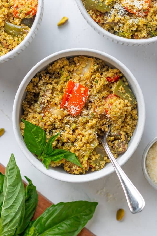 Bowls of cooked grains tossed in pesto with cooked veggies in it.