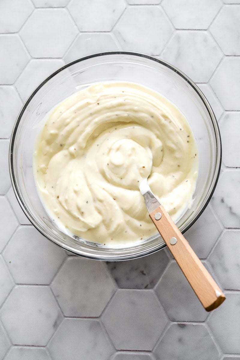 Creamy Greek yogurt potato salad dressing in a bowl with a spoon with a wood handle in the bowl.