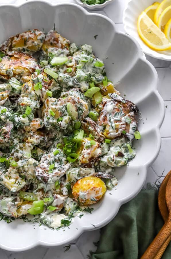 Serving bowl filled with crispy mixed potato salad with a bowl of sliced lemons and wood serving spoons next to it.