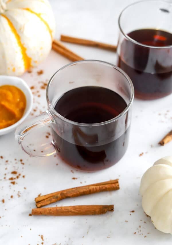 Brewed coffee in glass mugs with pumpkins and cinnamon sticks around it.