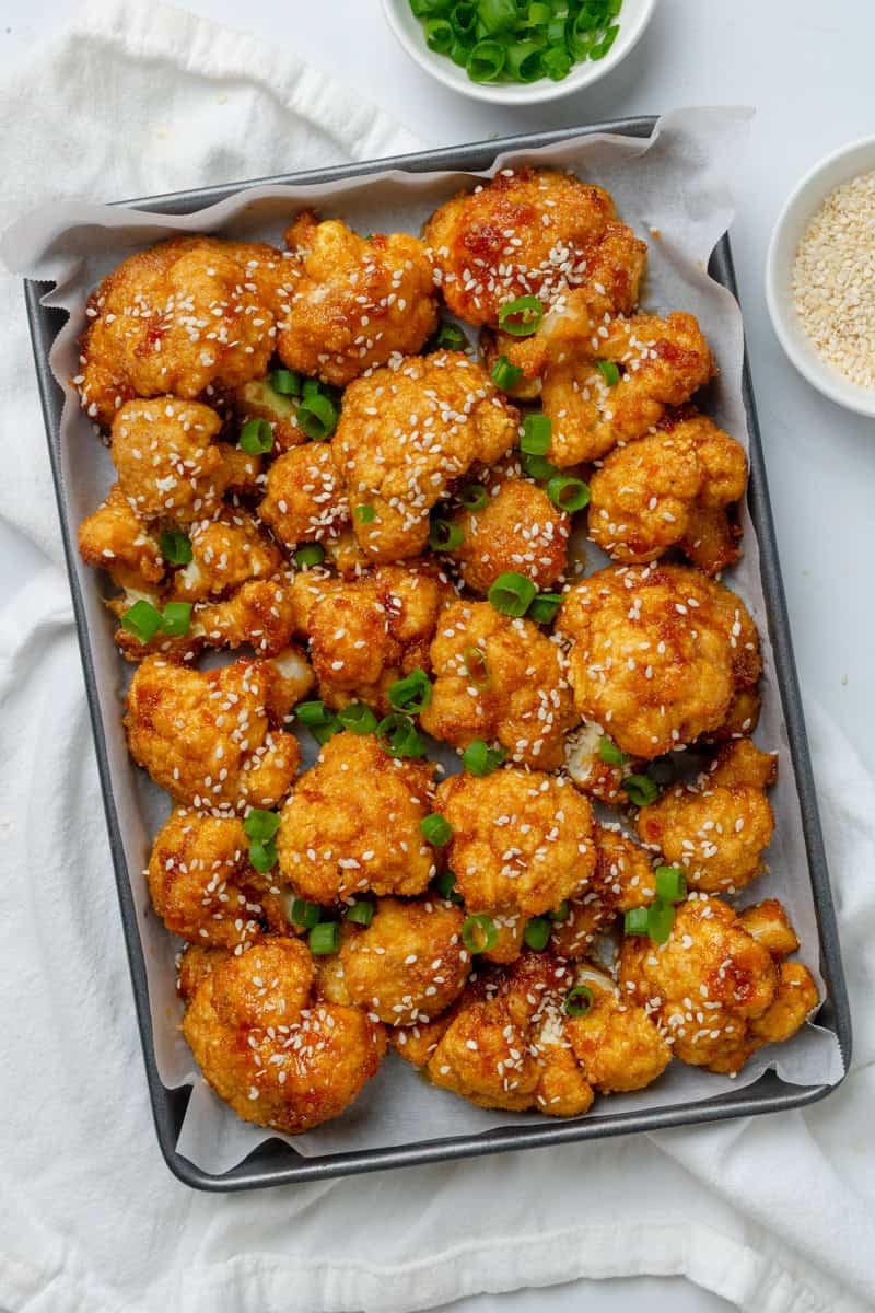 Pan loaded with golden oven fried crispy cauliflower wings with chopped scallions on top of them.