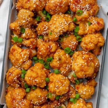 Baked cauliflower wings on a baking pan with chopsticks next to it.