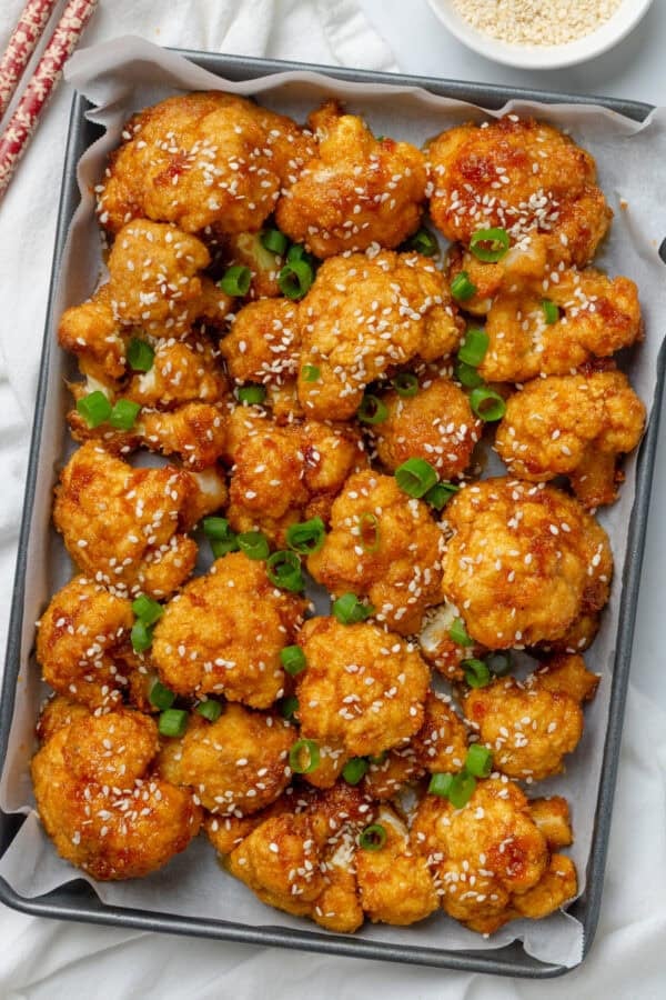 Baked cauliflower wings on a baking pan with chopsticks next to it.