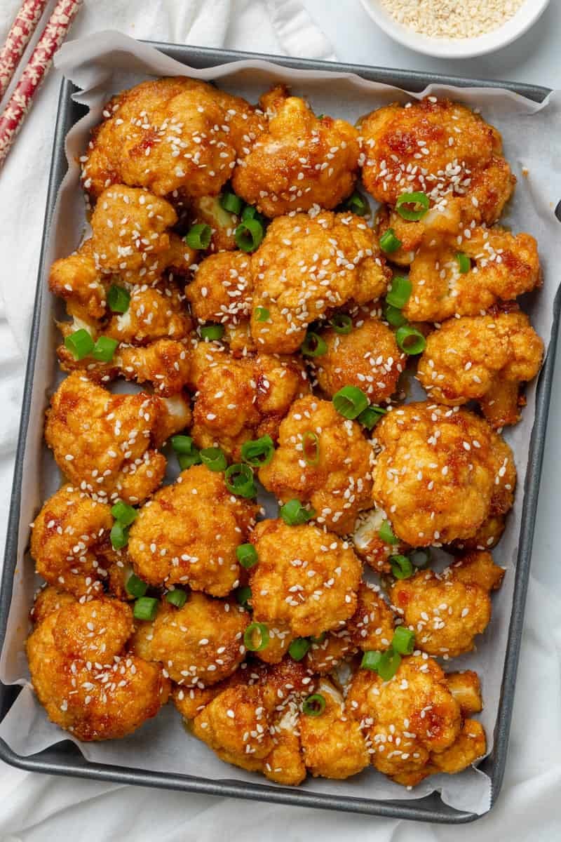 Baked cauliflower wings on a baking pan with chopsticks next to it. 