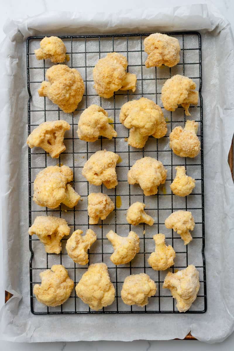 Coated cauliflower florets on a rack lined baking pan.