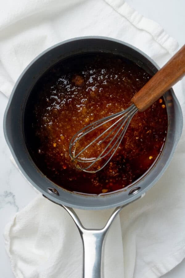 Blended sweet and spicy sauce in pan with a whisk in the pan with the sauce.