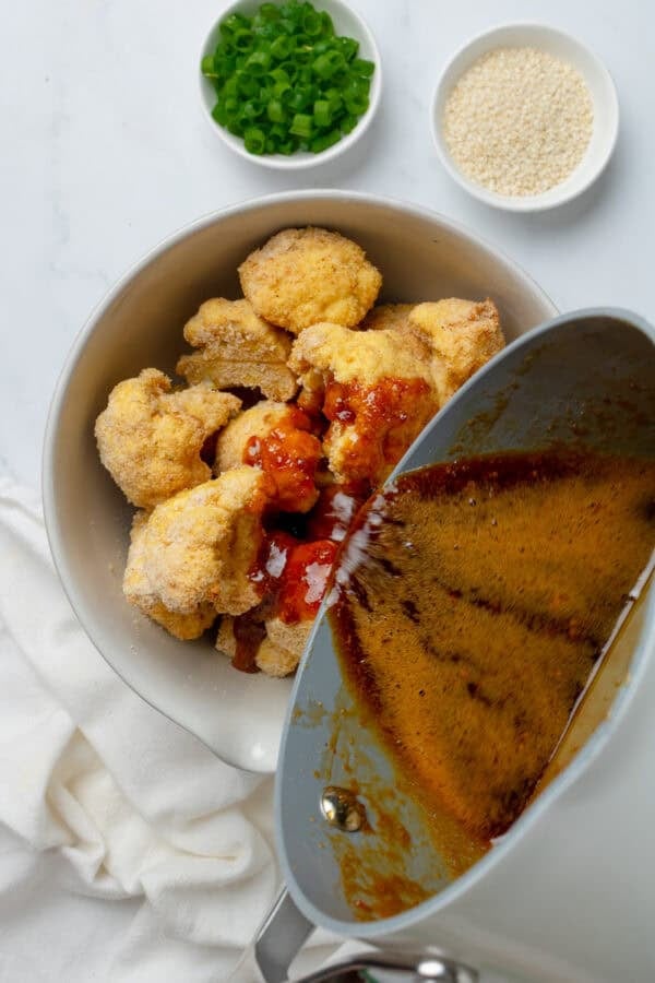 Pouring sauce onto baked coated cauliflower bites.