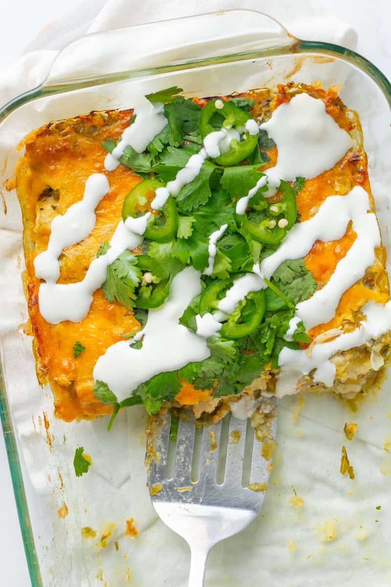 Glass pan of chicken enchiladas bake with some cut out of the pan. 