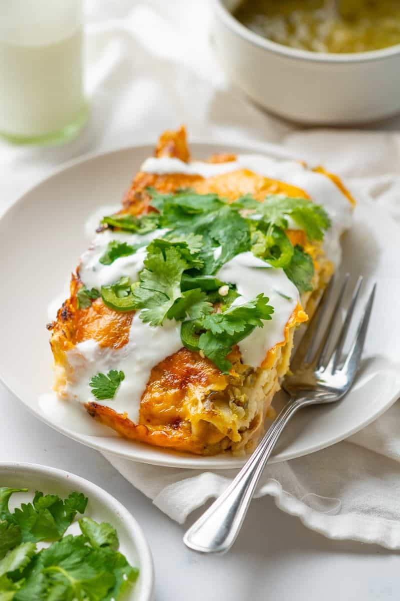 Plate with a serving of chicken enchiladas covered in melted cheese , topped with sour cream and shredded cilantro. 