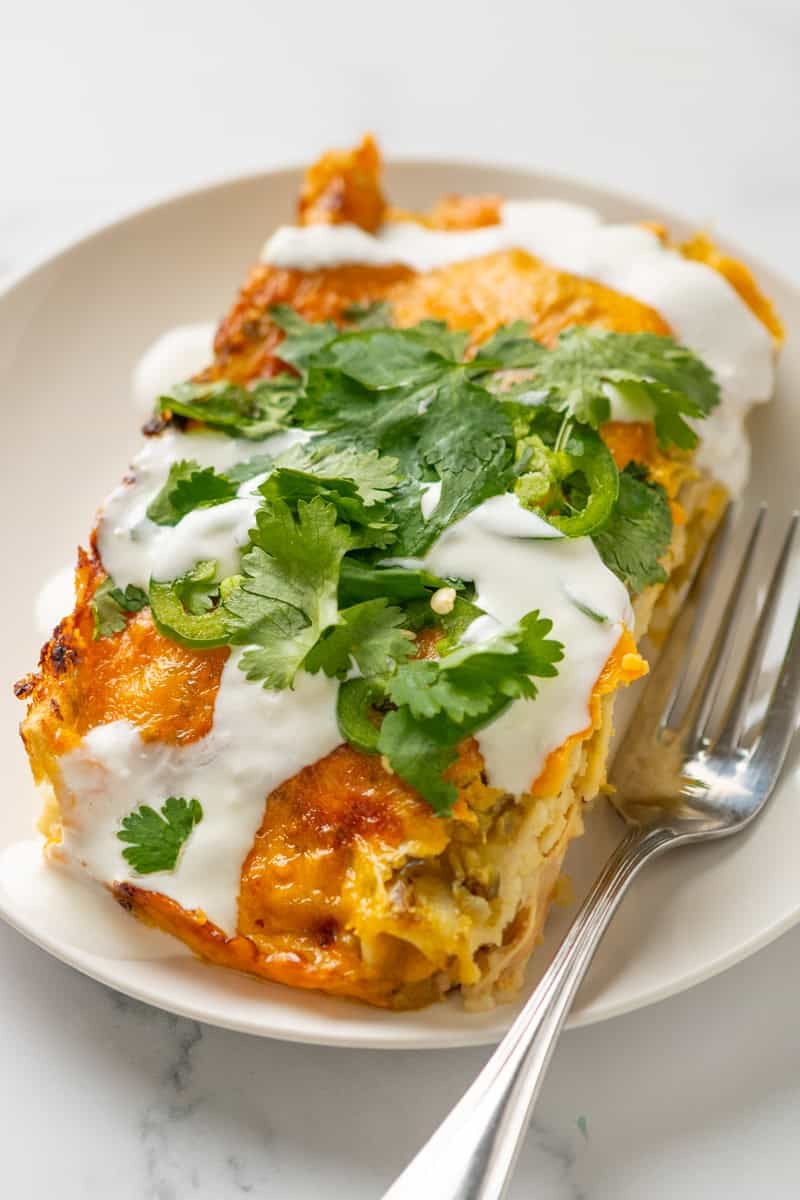 Plate of green chicken enchiladas with a fork next to it. 