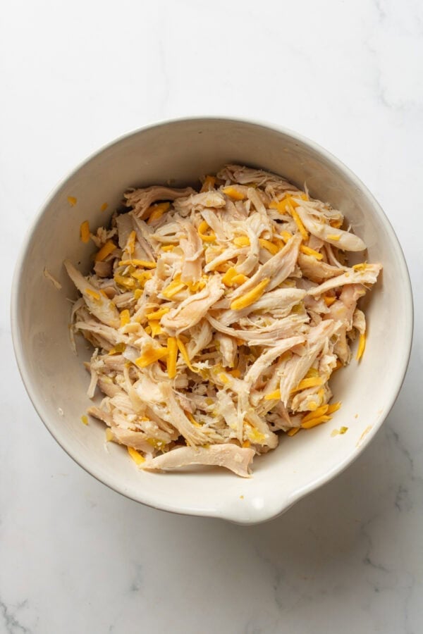 Bowl filled with cooked shredded chicken mixed with shredded cheddar cheese.