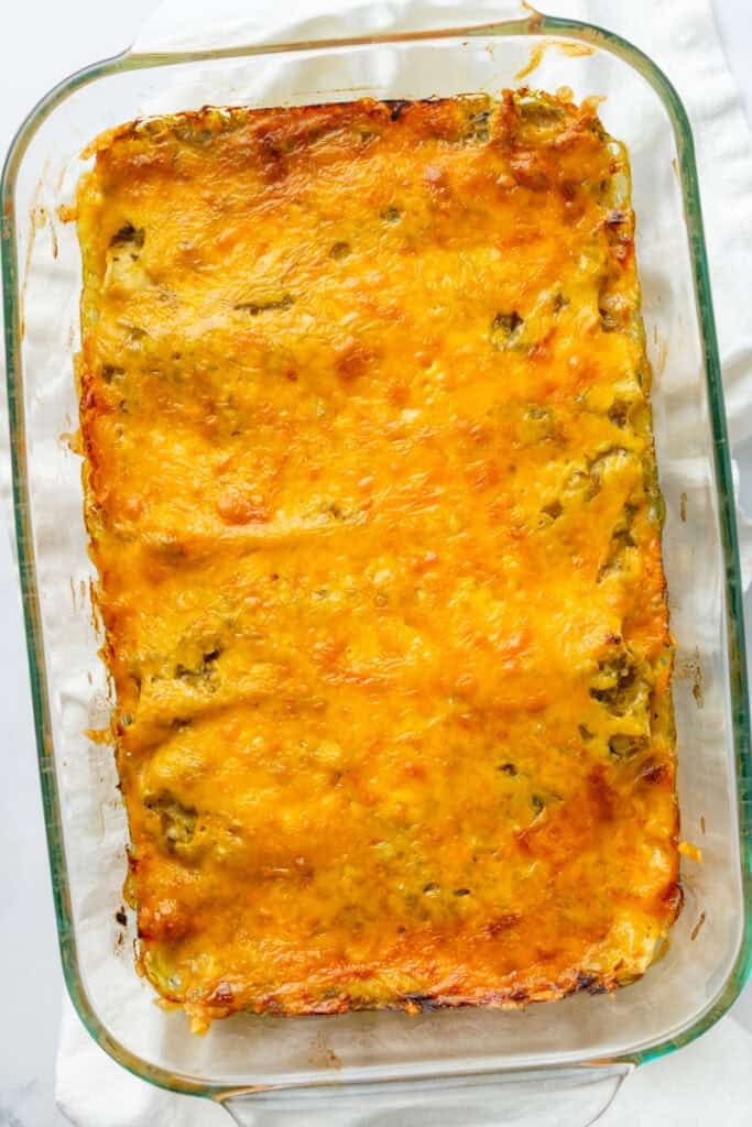 Glass pan of cooked chicken enchiladas with melty cheddar cheese on top.