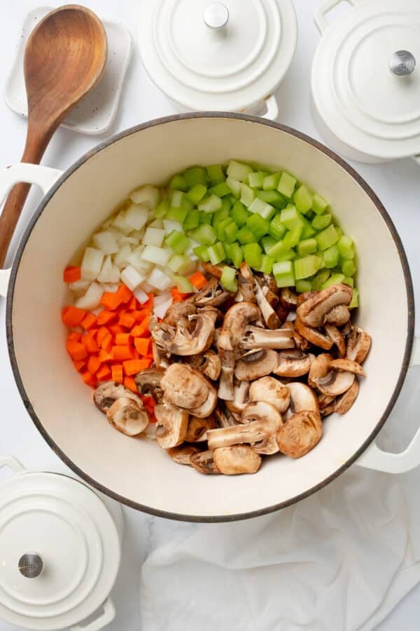 Veggies uncooked in a white pot with more ambler white pots around it.