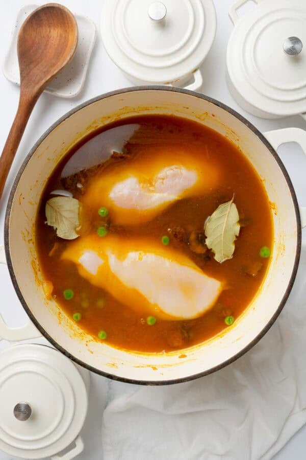 White soup pot with broth and chicken in it with a few small white pots around it.