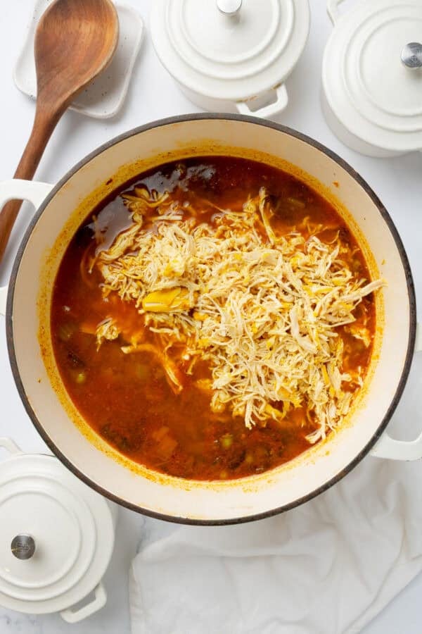 Cooked shredded chicken in a pot of soup in a white pot.