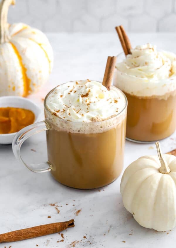 Glass mugs of coffee latte topped with whipped cream and a cinnamon stick.
