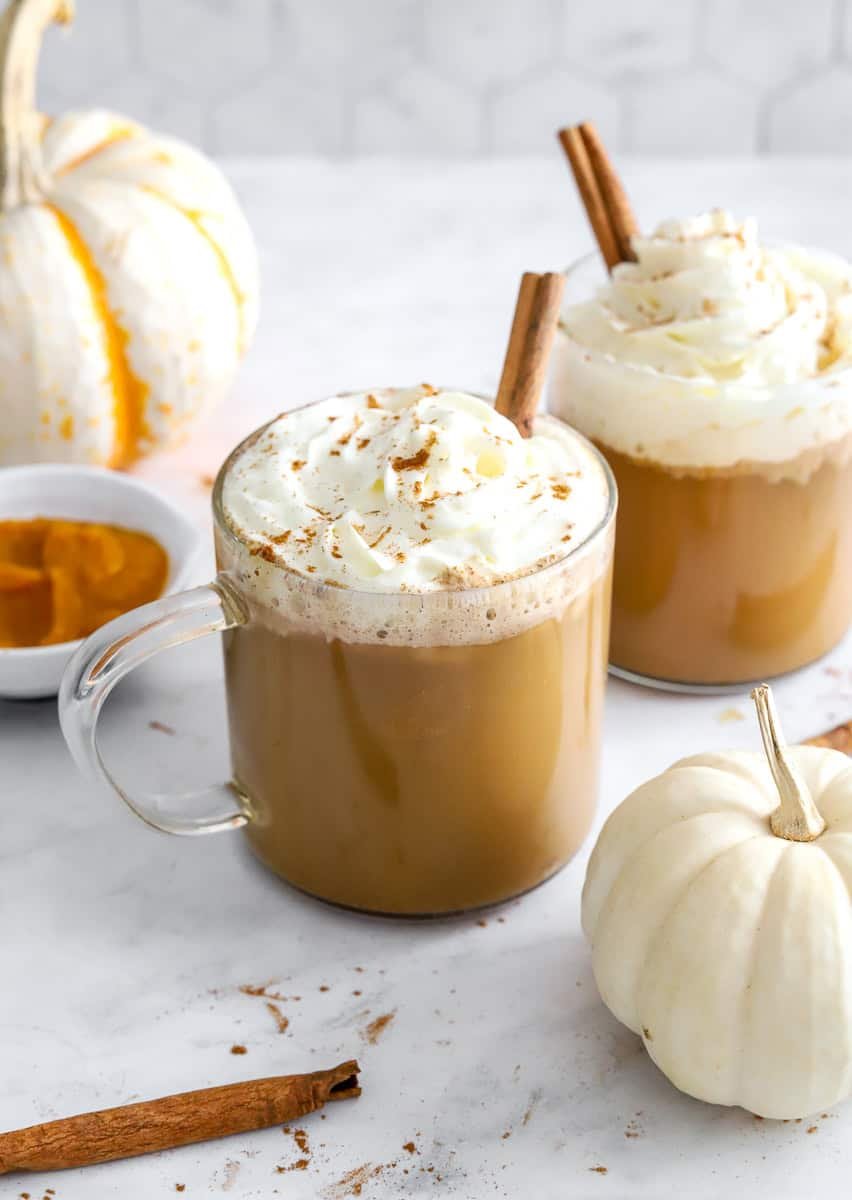 Glass mugs of coffee latte topped with whipped cream and a cinnamon stick. 