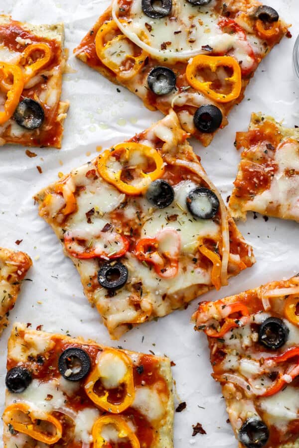 Squares of cooked chicken pizza topped with cheese and veggies.