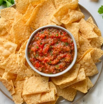 Tomato salas in a bowl on a platter with tortilla chips around it.