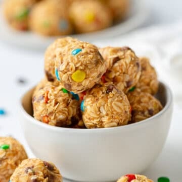 Bowl filled with monster cookie energy balls with more around it.
