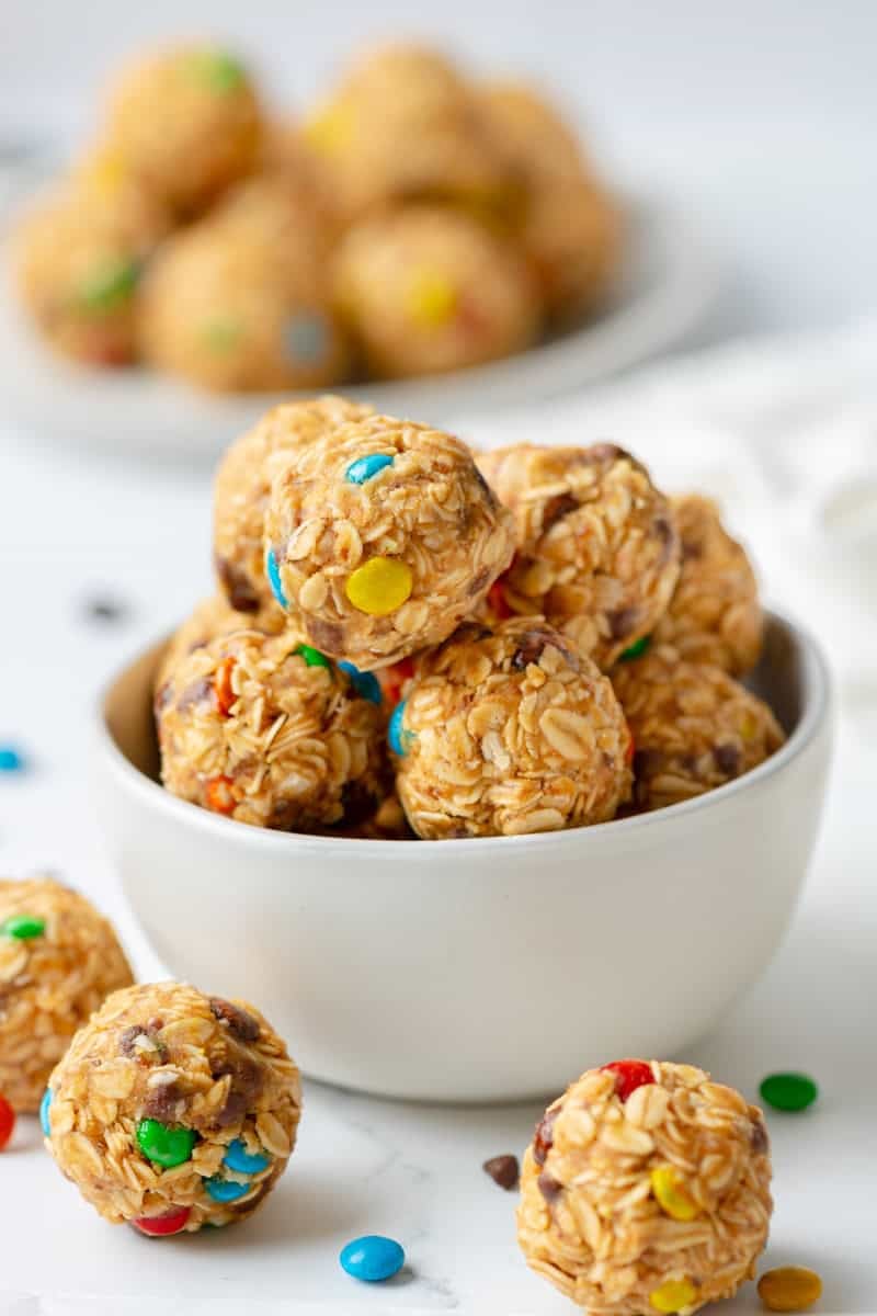 White bowl filled with monster cookie energy balls with more around it and behind it. 