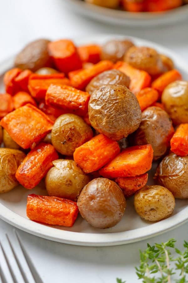 Cooked carrots and baby potatoes on a plate with herbs and a fork in front of it.