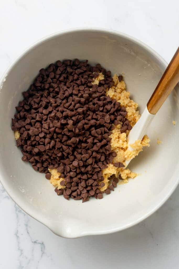 Mixing bowl with protein cookie dough with a pile of chocolate chips in it. 