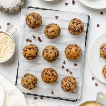 Rolled cookie dough balls on a lined rack with more recipe ingredients in bowls around it.