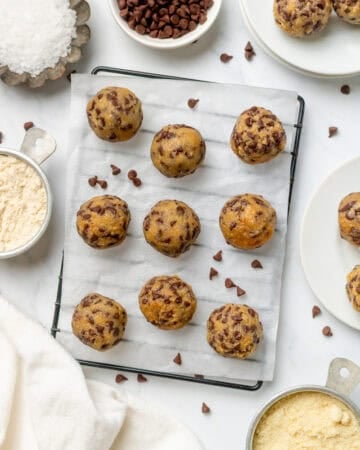 Rolled cookie dough balls on a lined rack with more recipe ingredients in bowls around it.