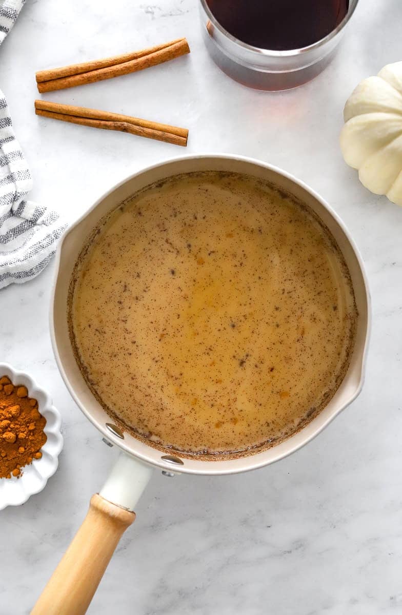 Pumpkin spice latter creamer in a pot with pumpkin spice in a bowl in front of it and cinnamon sticks behind it.