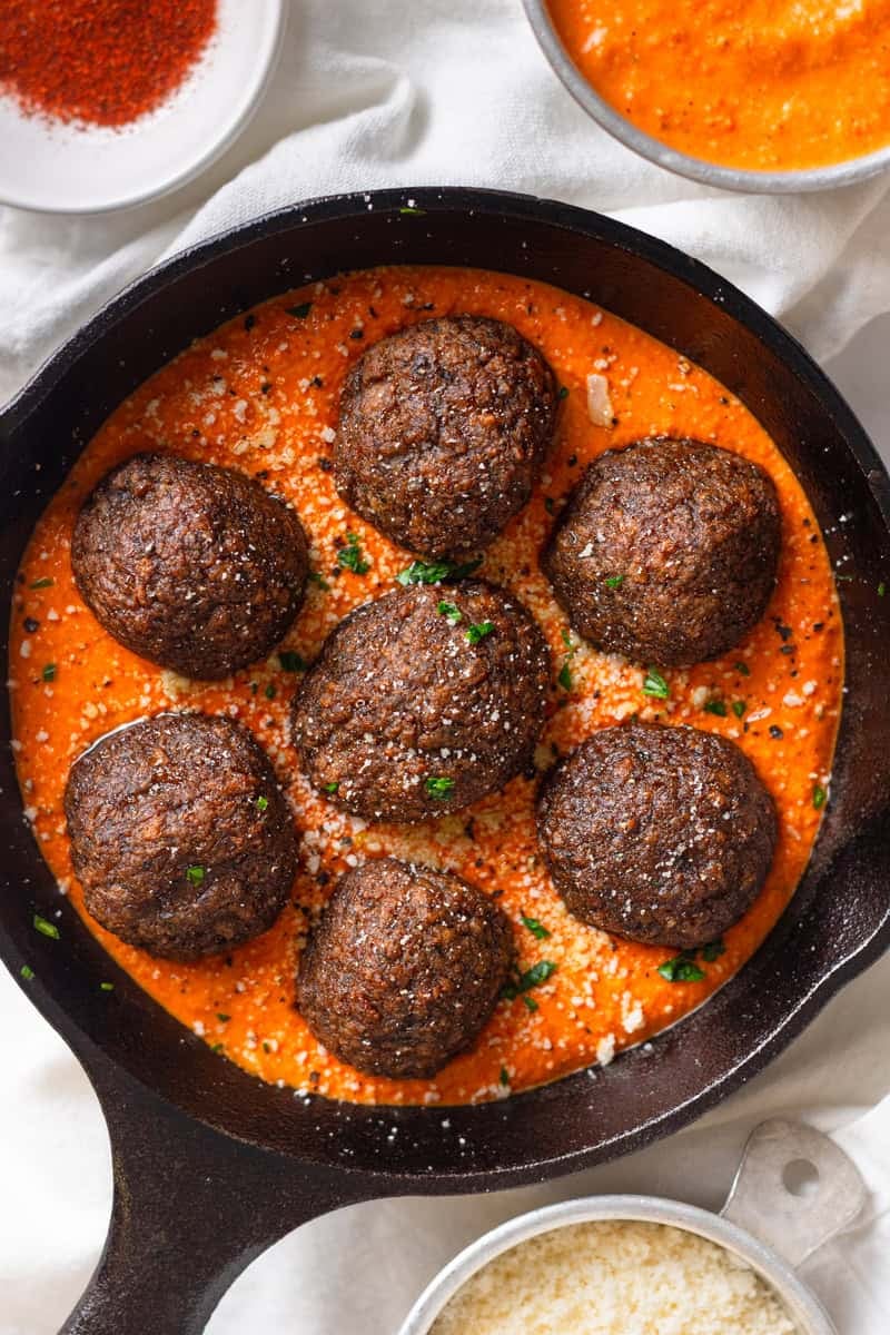 Cast iron pan filled with meatballs in orange romesco sauce.