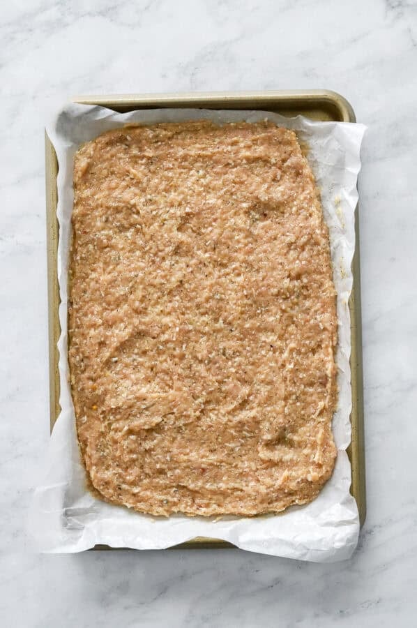 Uncooked chicken crust spread out on lined pan.