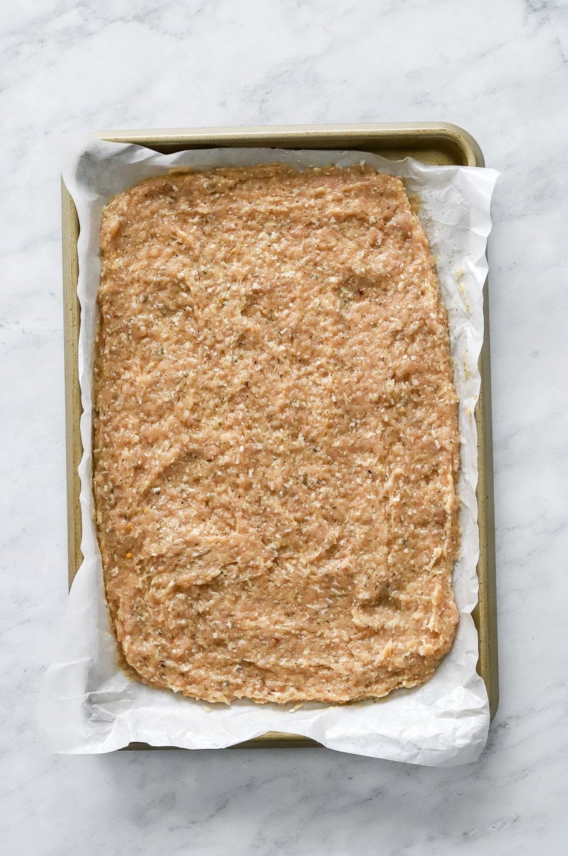 Uncooked chicken crust spread out on lined pan.