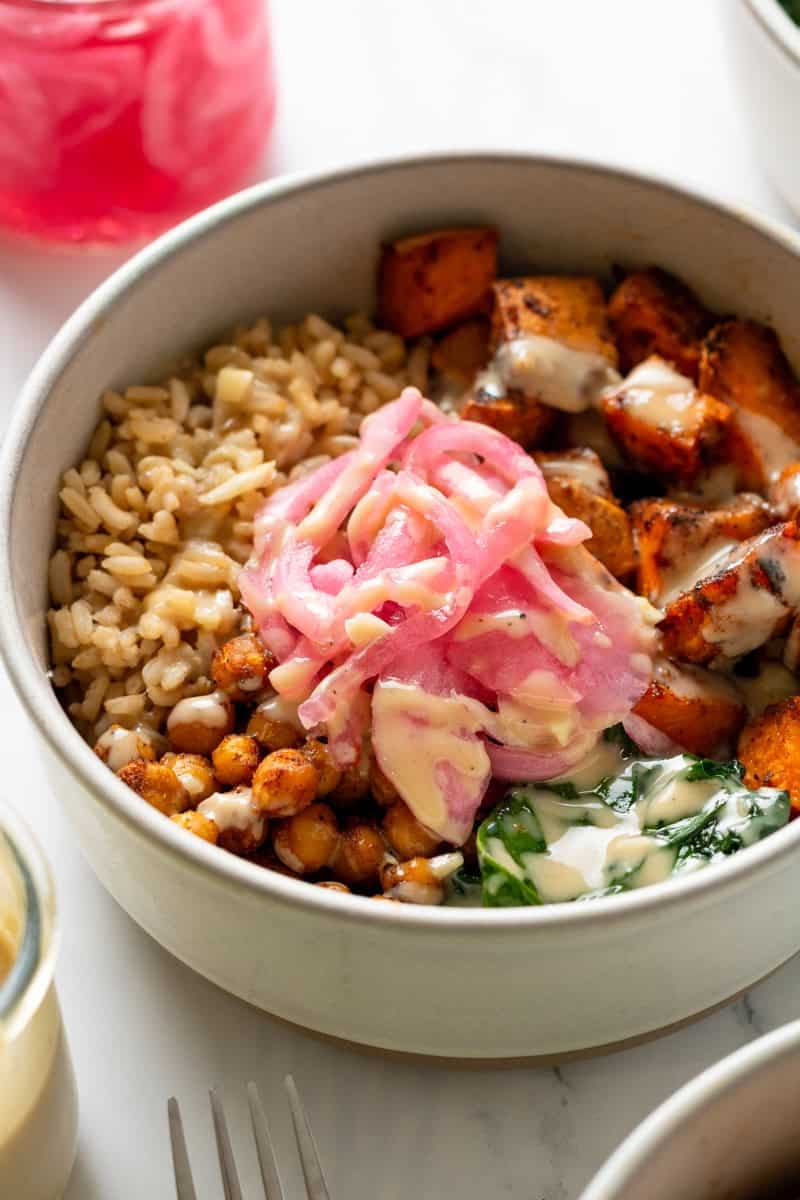 Sweet potato chickpea bowl with red onion and spinach in a bowl with ingredients around it.