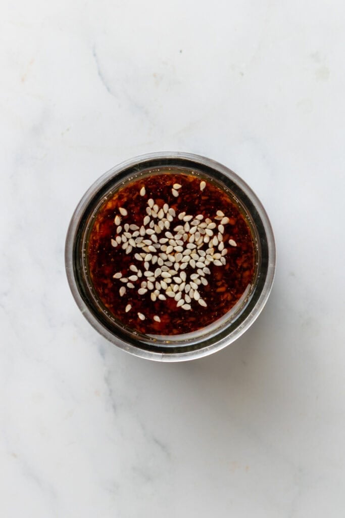 Egg roll sauce mixes up in mason jar with sesame seeds on top of it.