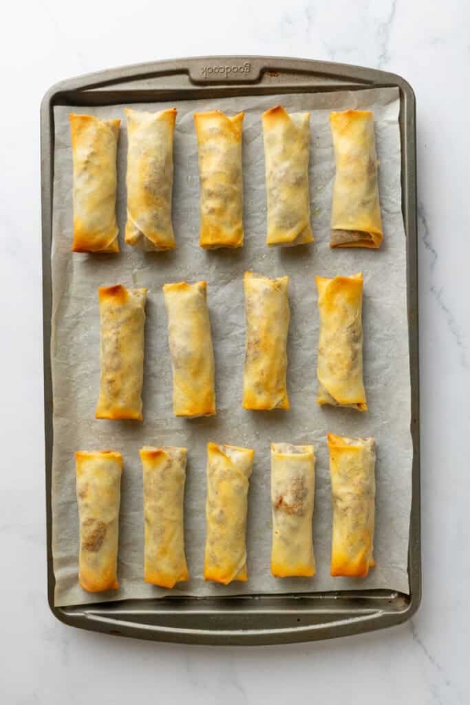 Baked veggie and tofu egg rolls on a lined baking pan.
