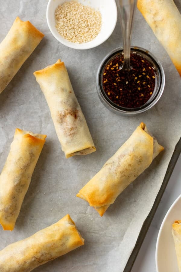 Cooked veggie egg rolls on a pan with dipping sauces.
