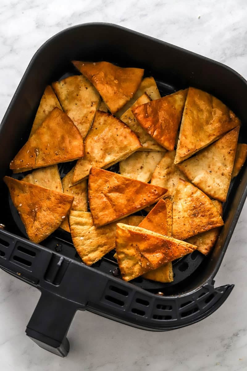 Cooked pita chips in black air fryer basket.