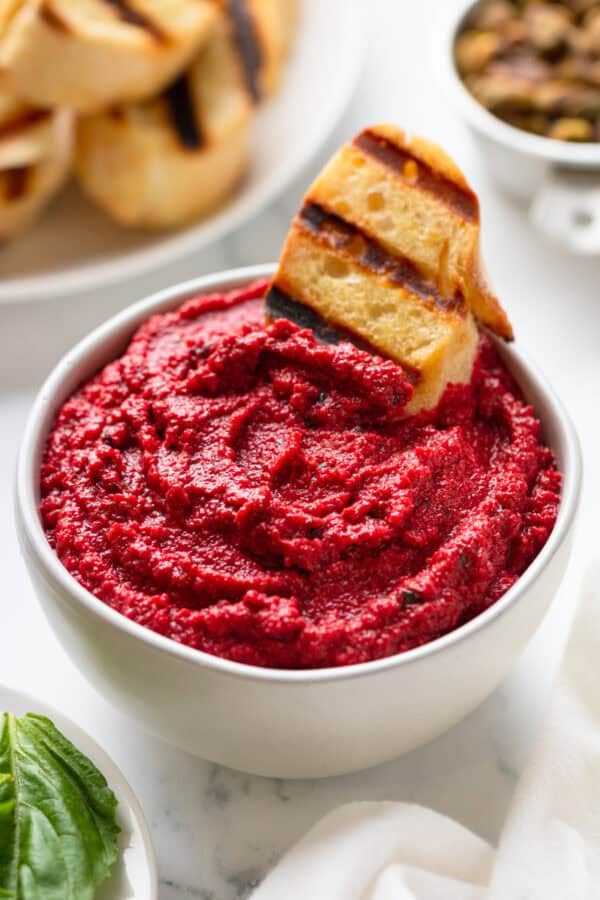 Pink sauce from beets in a white bowl with a piece of grilled crostini in it.