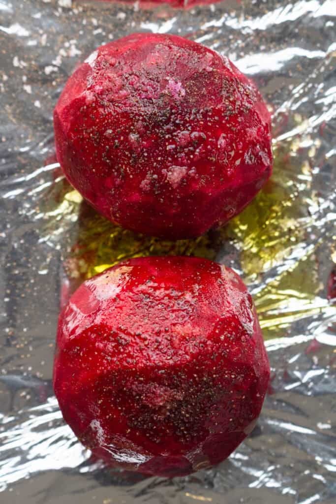 Peeled uncooked beets covered in oil and salt on some foil.