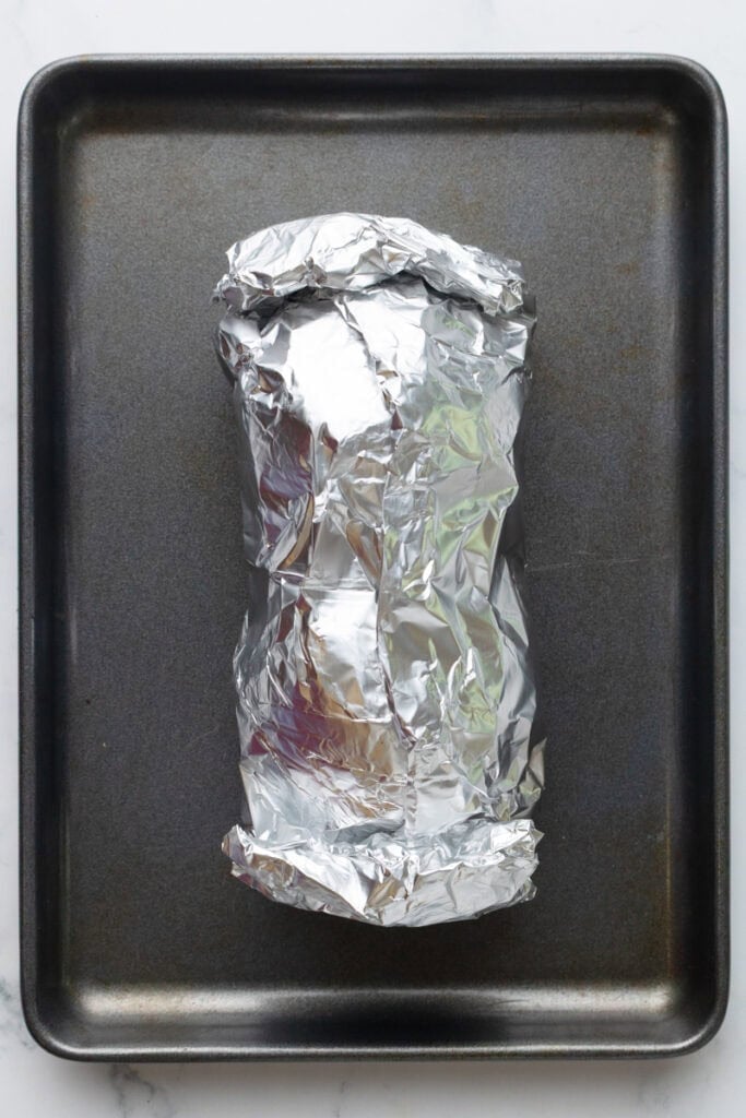 Beets covered in foil on a baking pan.