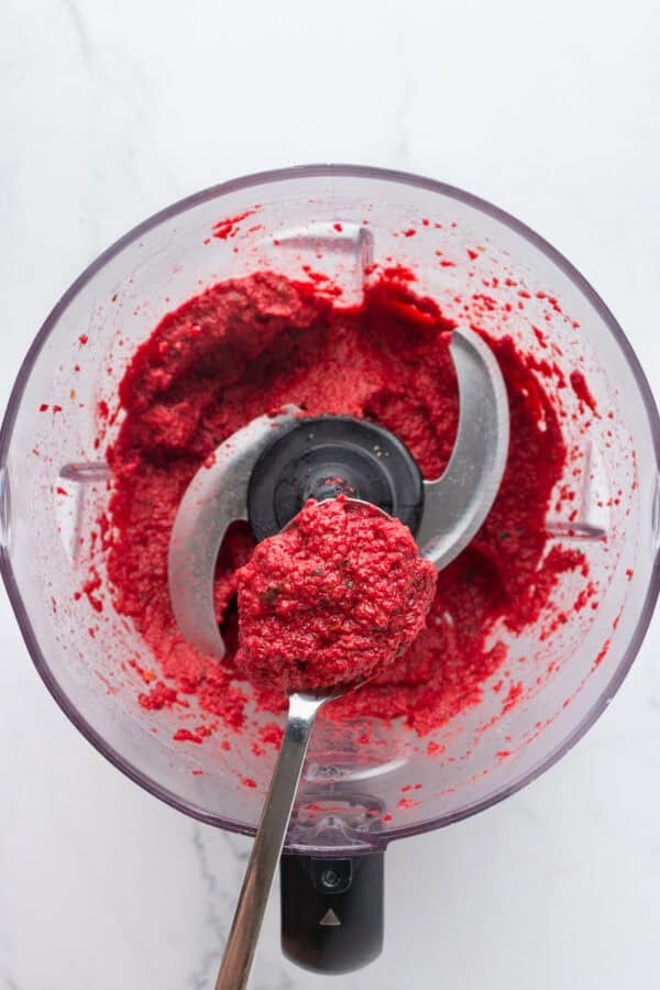 Beet pesto blended in a food processor with a spoon with some on it over it.